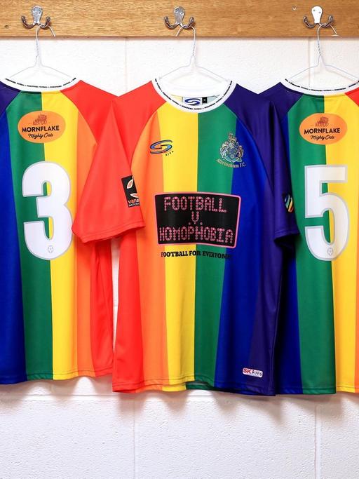 Fußballertrikots in den Farben des Regenbogens hängen in einer Kabine