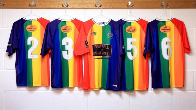 Fußballertrikots in den Farben des Regenbogens hängen in einer Kabine
