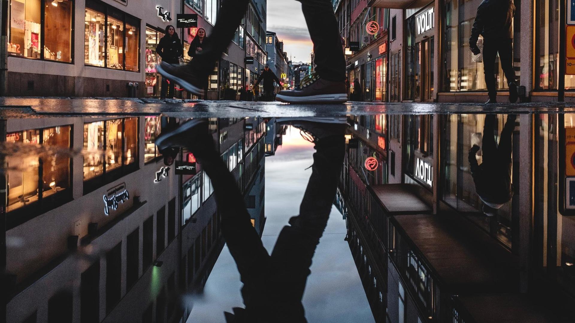 Nahaufnahme eines Fußgängers, dessen Beine sich in einer Pfütze spiegeln. Nahaufnahme eines Fußgängers, dessen Beine sich in einer Pfütze spiegeln.