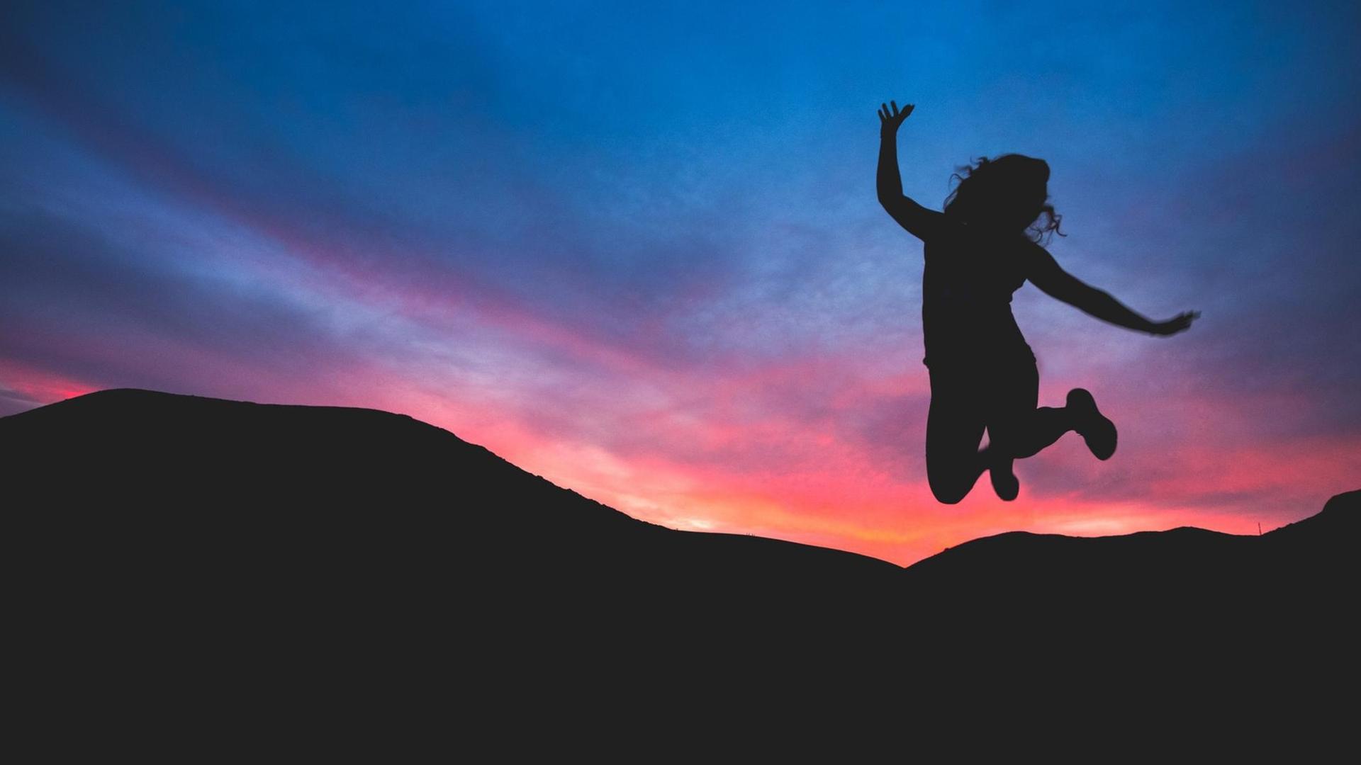 Eine Frau macht einen Luftsprung. Im Hintergrund: Sonnenuntergang und Berge. Eine Frau macht einen Luftsprung. Im Hintergrund: Sonnenuntergang und Berge.