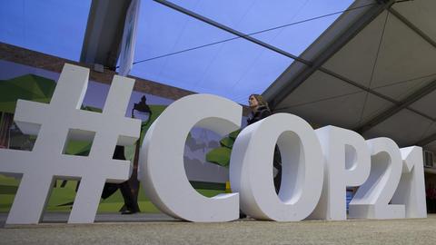 Ein Mann läuft an den etwa einen Meter hohen Zeichen "#COP21" vorbei, die als Installation im Raum stehen.