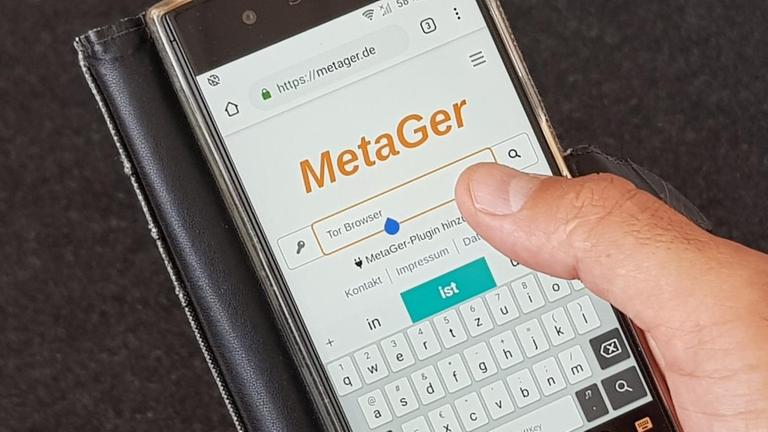 Eine Hand hält ein Smartphone, auf dem MetaGer zu sehen ist, eine deutsche Metasuchmaschine im Internet.