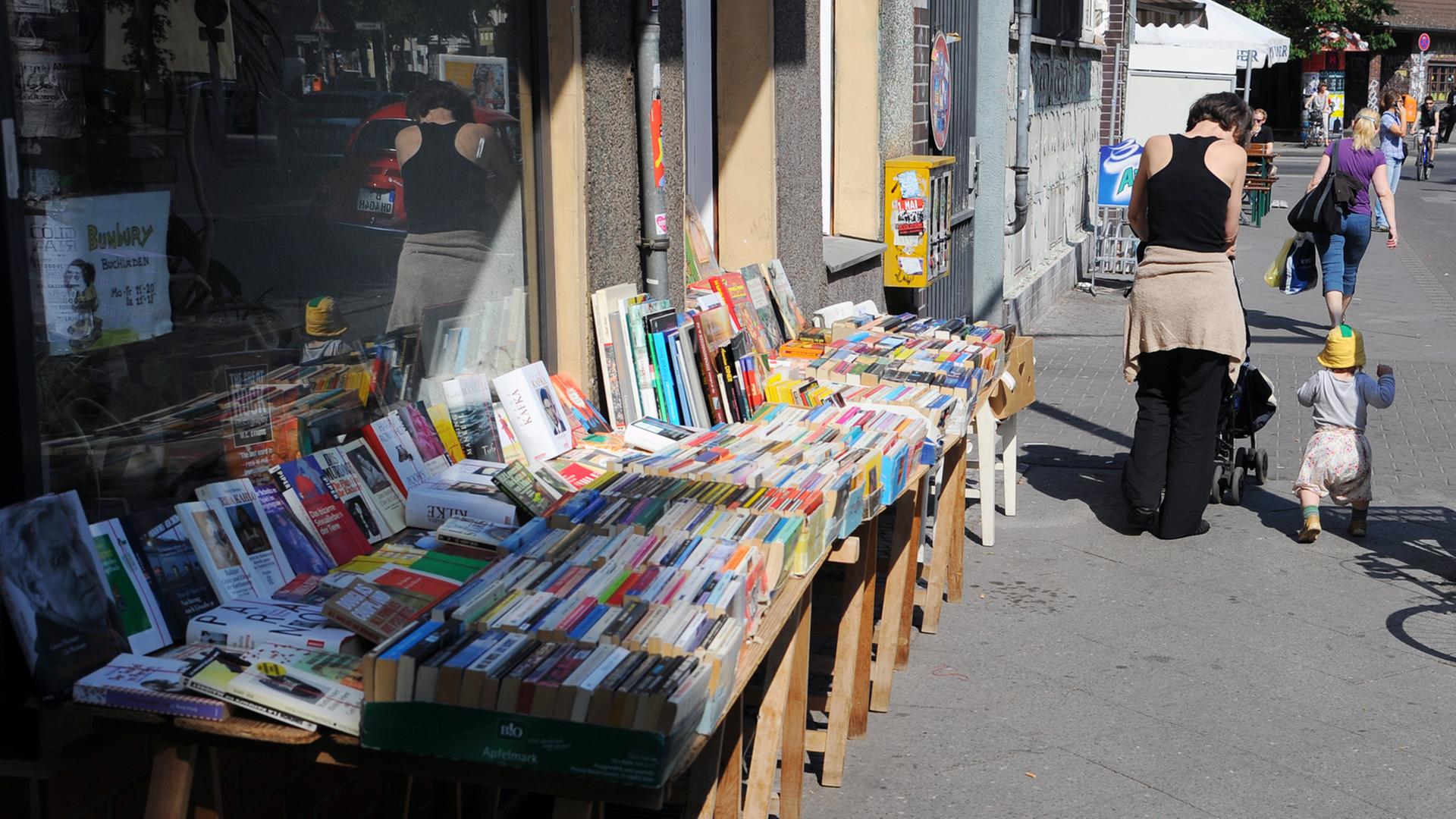 Eine Mutter mit Kleinkind geht an einem Buchladen mit gebrauchten Büchern in der Weserstraße in Berlin-Neukölln vorbei, aufgenommen 2012 Eine Mutter mit Kleinkind geht an einem Buchladen mit gebrauchten Büchern in der Weserstraße in Berlin-Neukölln vorbei, aufgenommen 2012