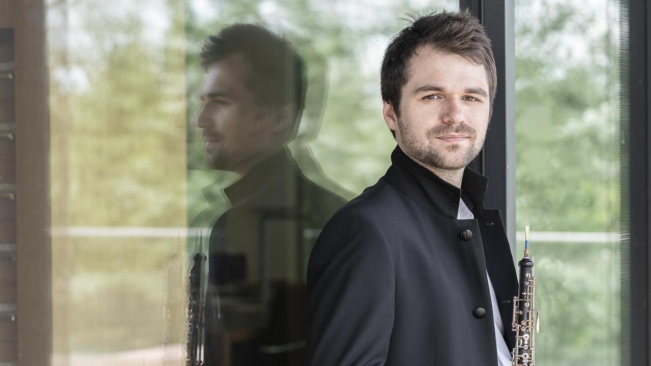Der Musiker steht mit hochgeschlagenem Mantelkragen und Instrument vor einer Glastür Der Musiker steht mit hochgeschlagenem Mantelkragen und Instrument vor einer Glastür