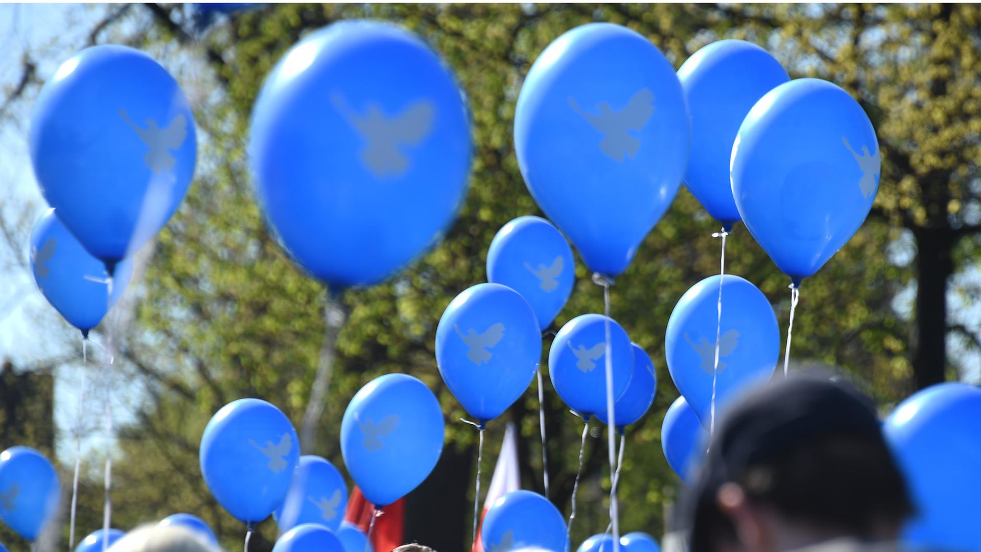 Teilnehmer des Ostermarsches halten in Wedel (Schleswig-Holstein) blaue Luftballons mit einer Friedenstaube hoch.