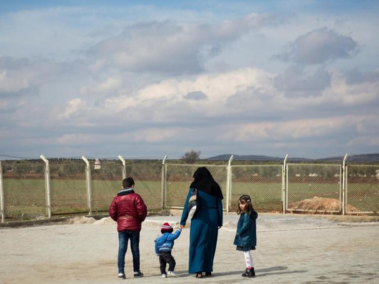 Eine syrische Flüchtlingsfamilie steht am Grenzzaun zum Nachbarland Türkei in der Nähe der türkischen Stadt Kilis