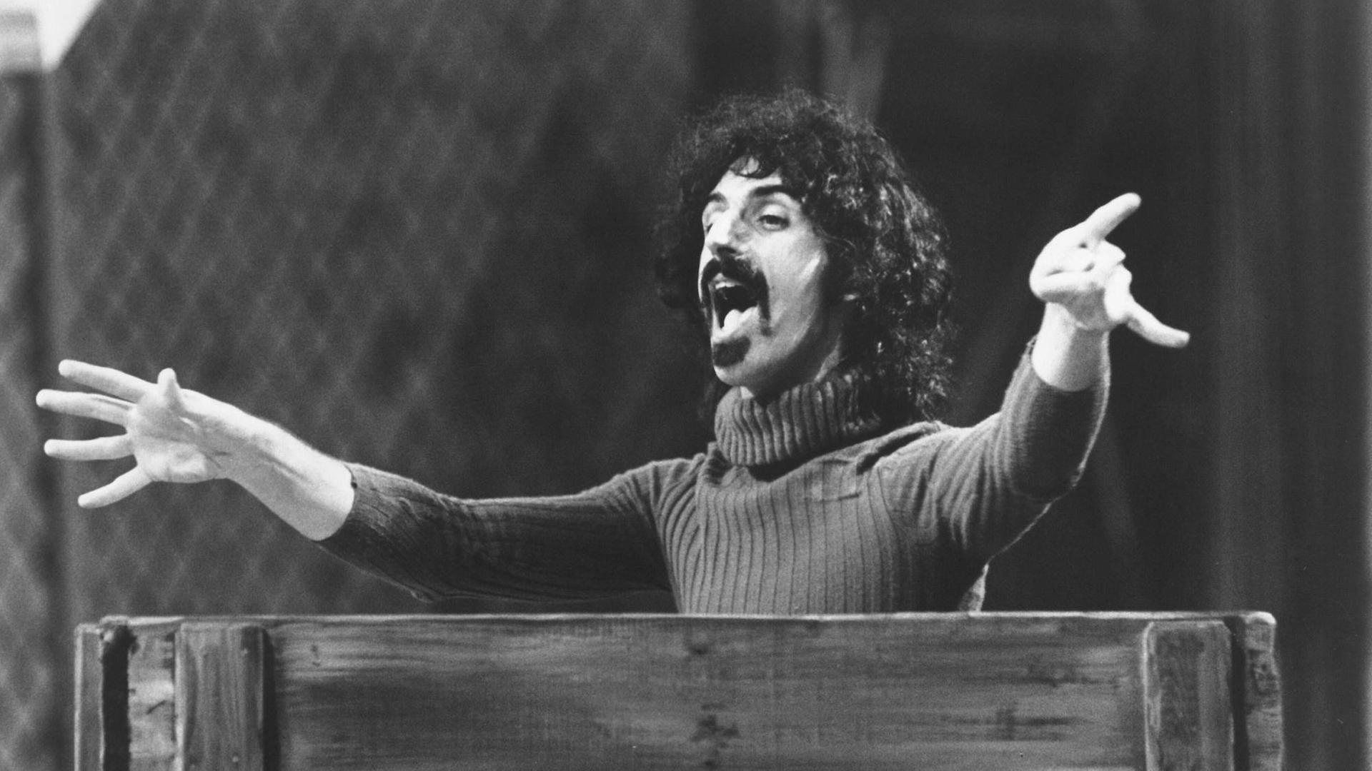 Frank Zappa steht hinter einem Pult in Dirigentenpose. Frank Zappa steht hinter einem Pult in Dirigentenpose.