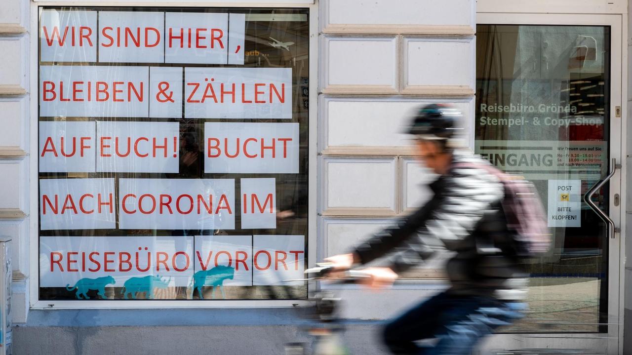 Ein Radfahrer fährt am Schaufenster eines Reisebüros vorbei. Nach wochenlanger Zwangsschließung wegen der Corona-Schutzmaßnahmen dürfen vom 20.04.2020 an Geschäfte des Einzelhandels wieder öffnen. Ein Radfahrer fährt am Schaufenster eines Reisebüros vorbei. Nach wochenlanger Zwangsschließung wegen der Corona-Schutzmaßnahmen dürfen vom 20.04.2020 an Geschäfte des Einzelhandels wieder öffnen.