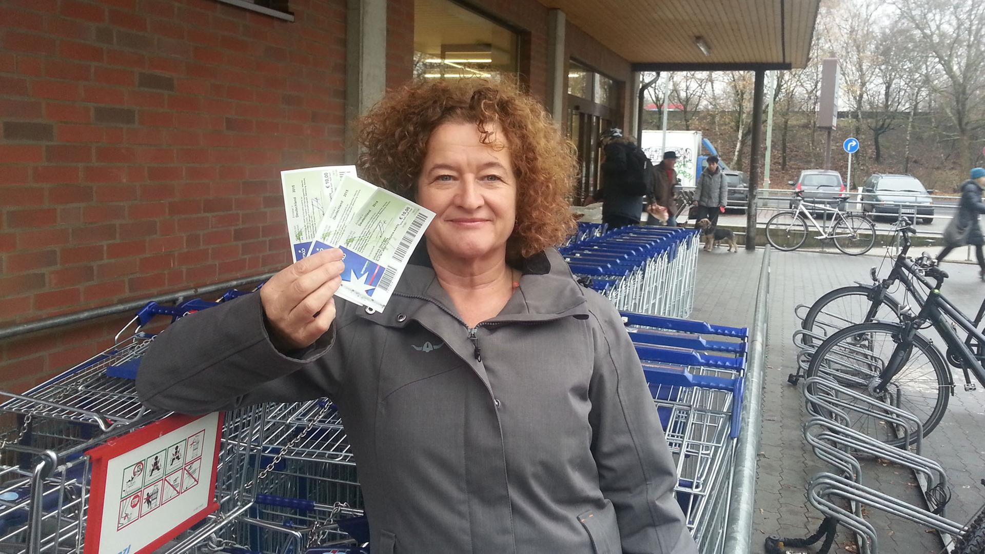 Autorin Ellen Häring hält vor einem Supermarkt Gutscheine im Wert von 30 Euro in der Hand