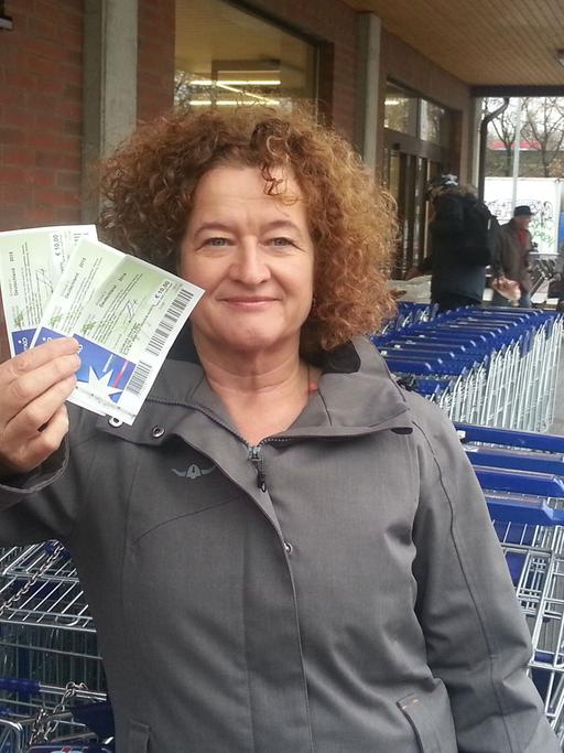 Autorin Ellen Häring hält vor einem Supermarkt Gutscheine im Wert von 30 Euro in der Hand