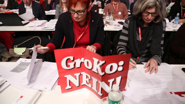 Bundesparteitag der SPD am 07.12.2017 in Berlin: Delegierte lesen in ihren Unterlagen hinter einem Schild "GroKo: Nein!"