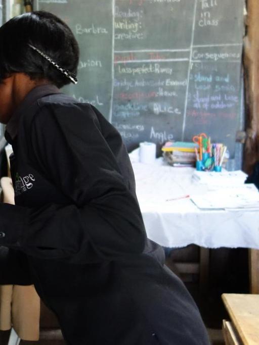 An "Bridge"-Schulen unterrichten die Lehrerinnen und Lehrer unterstützt durch Tablet-Computer. Hier eine Lehrerin in Kenia, die an der Tafel mit Kreide steht und in der anderen Hand ein Tablet hält.