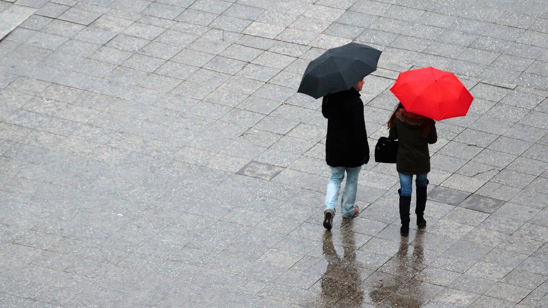 Ein Paar mit rotem und schwarzem Regenschirm flaniert in Frankfurt.