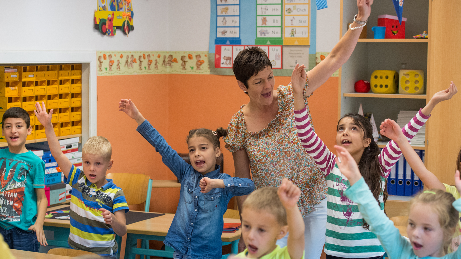 Grundschulkinder und eine Lehrerin singen und bewegen ihre Arme. Grundschulkinder und eine Lehrerin singen und bewegen ihre Arme.