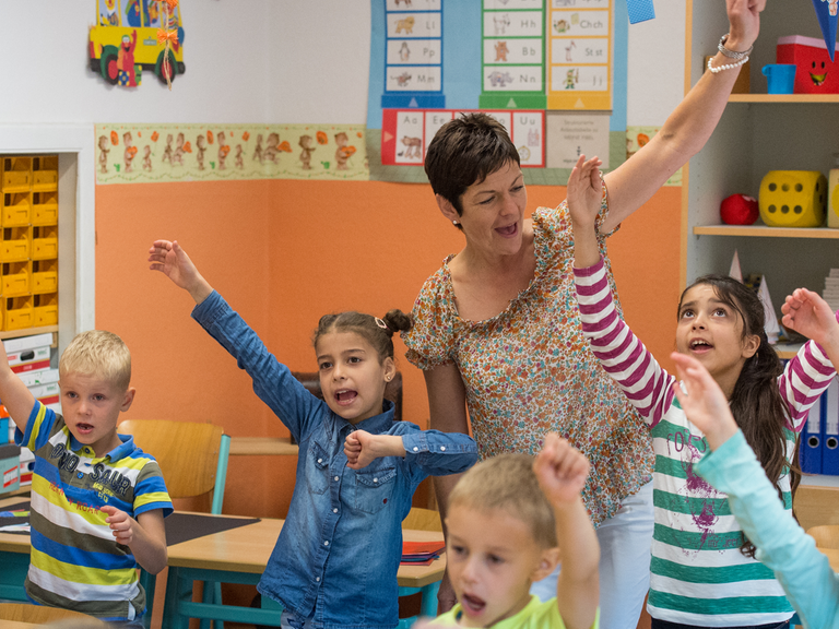 Grundschulkinder und eine Lehrerin singen und bewegen ihre Arme.