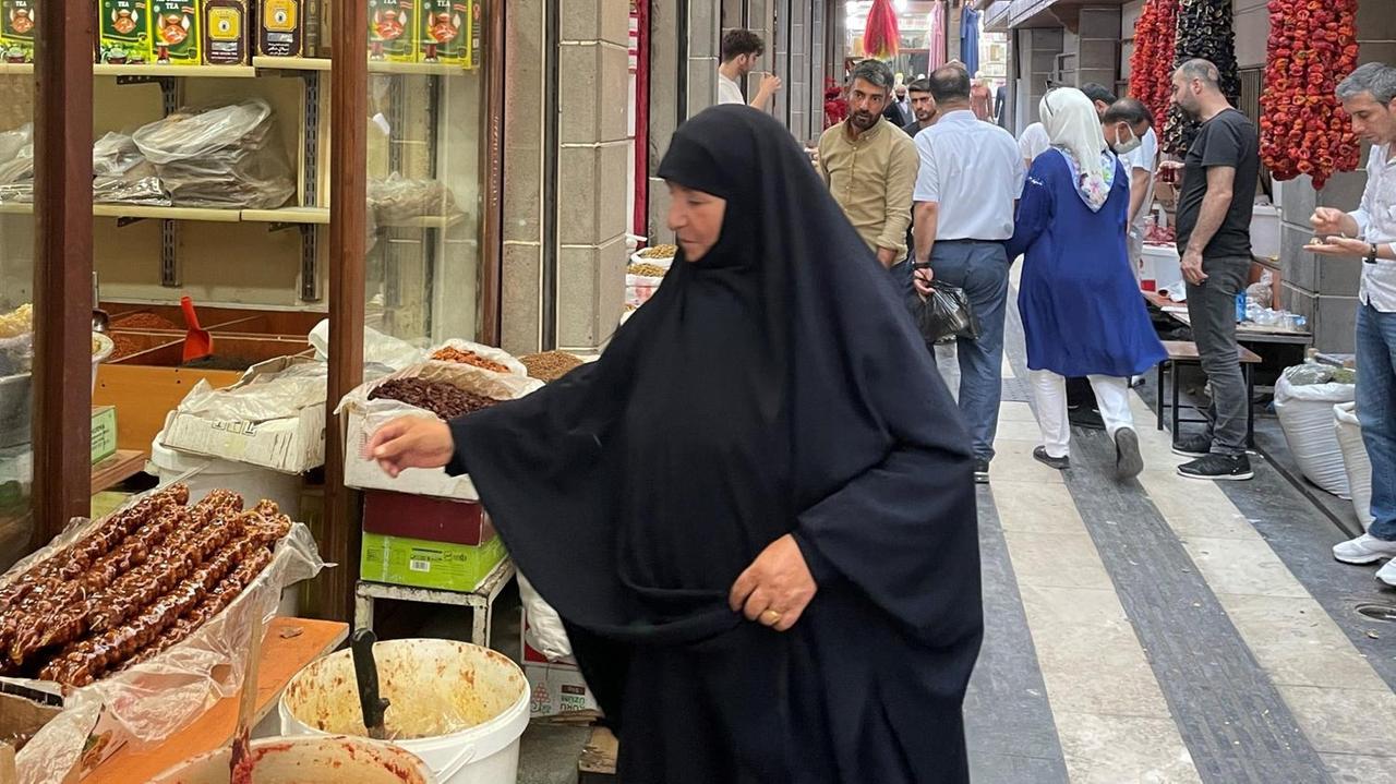 Eine ältere kräftige Frau im schwarzen Tschador begutachtet die Produkte an einem Marktstand. Eine ältere kräftige Frau im schwarzen Tschador begutachtet die Produkte an einem Marktstand.