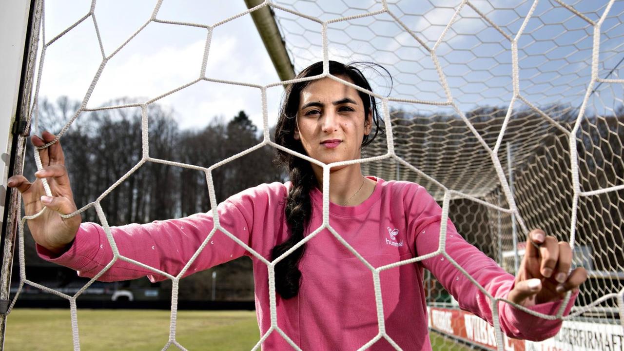 Die Fußballerin Khalida Popal blickt im Fußballdress durch ein Tornetz in ihrem Verein in Dänemark. Die Fußballerin Khalida Popal blickt im Fußballdress durch ein Tornetz in ihrem Verein in Dänemark.
