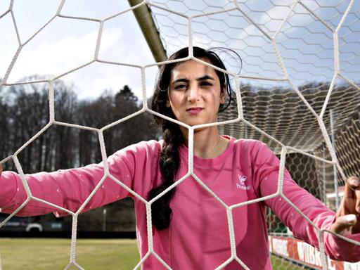 Die Fußballerin Khalida Popal blickt im Fußballdress durch ein Tornetz in ihrem Verein in Dänemark.