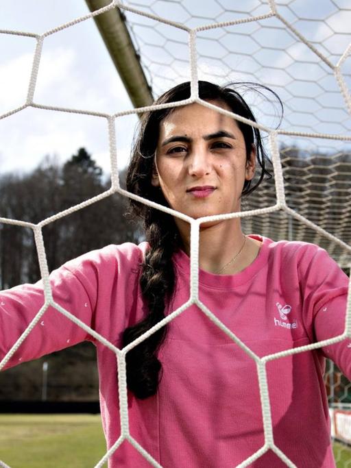 Die Fußballerin Khalida Popal blickt im Fußballdress durch ein Tornetz in ihrem Verein in Dänemark.