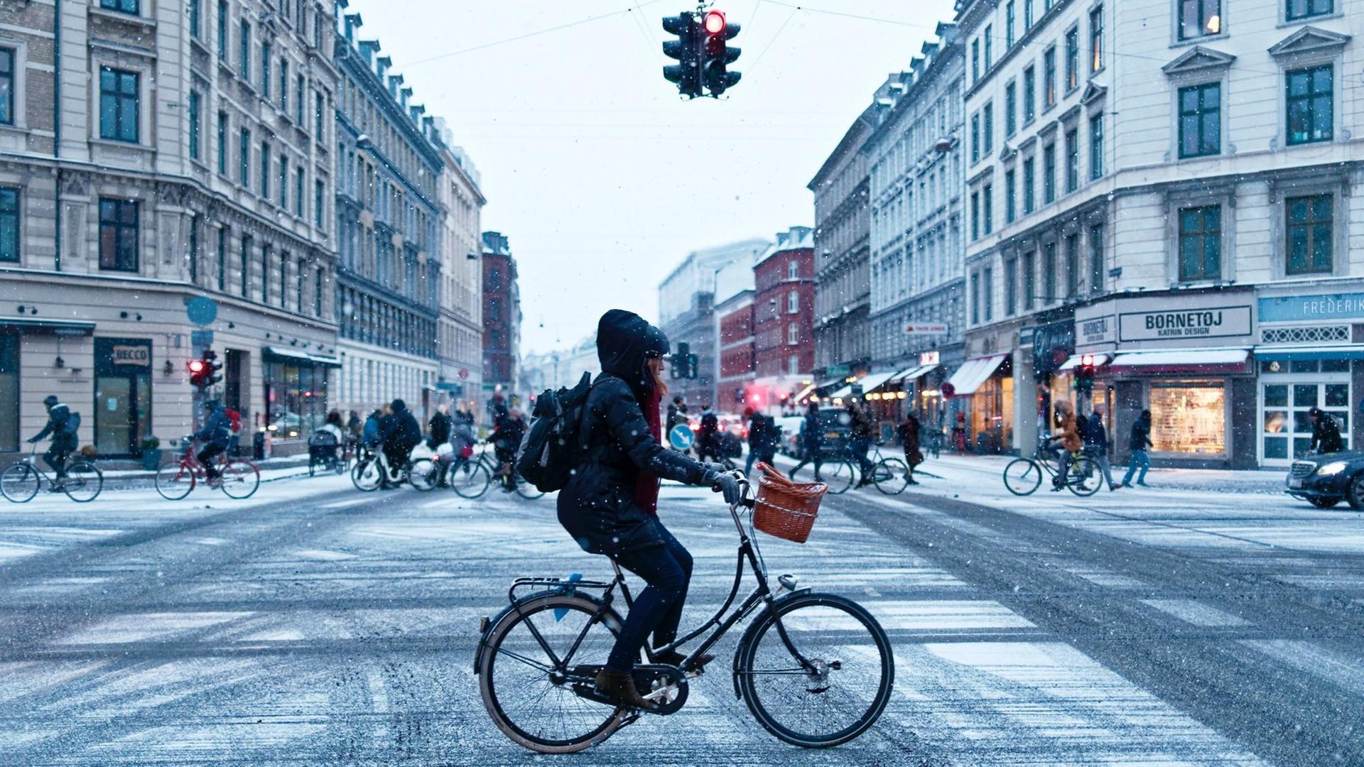 Eine Frau fährt mit dem Rad über eine verschneite Kreuzung.