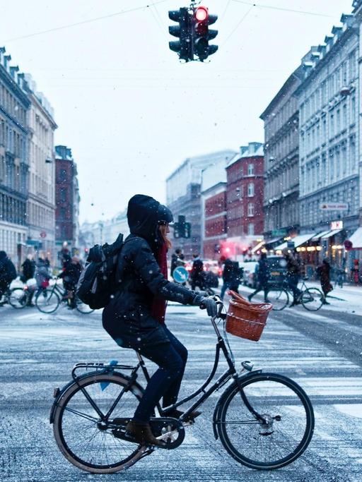 Eine Frau fährt mit dem Rad über eine verschneite Kreuzung.