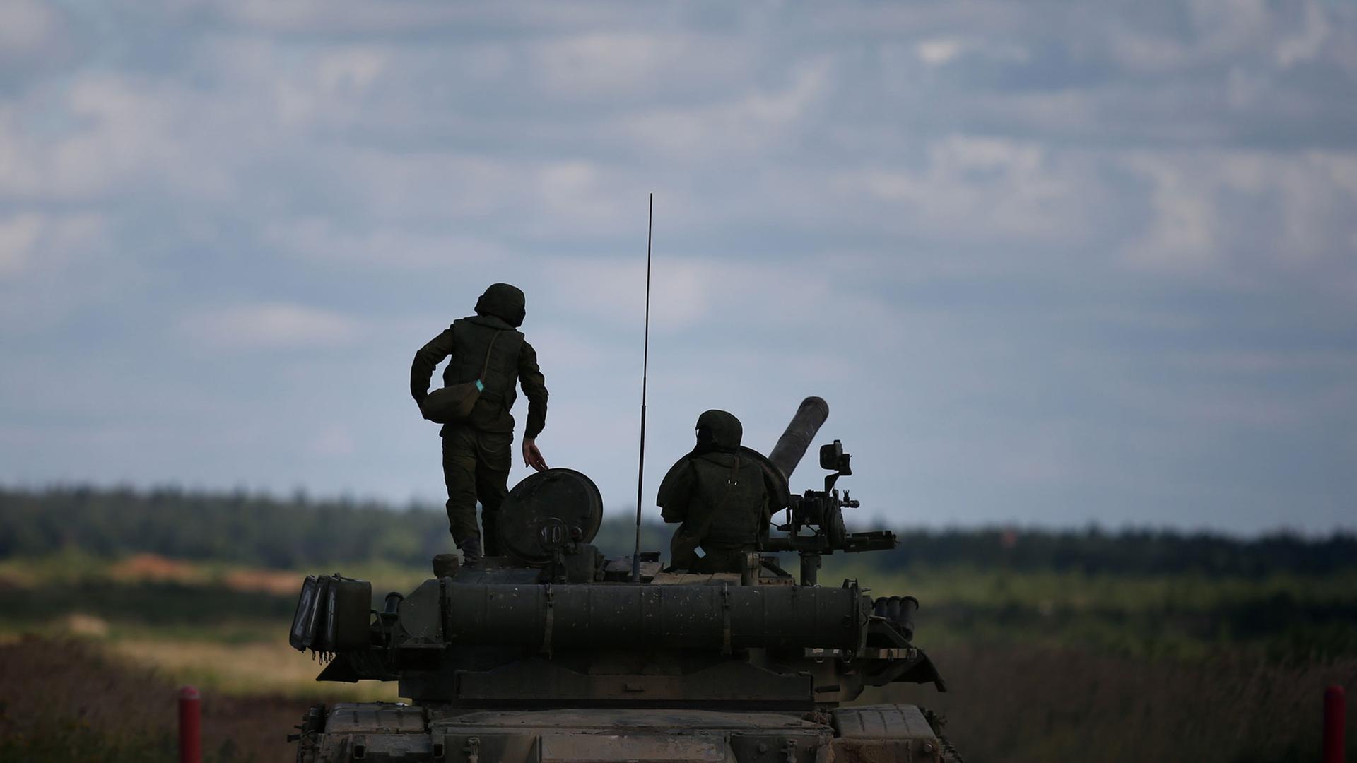Man sieht im Gegenlicht zwei Soldaten auf dem Panzer, der in einem Feld unter Wolkenhimmel steht.