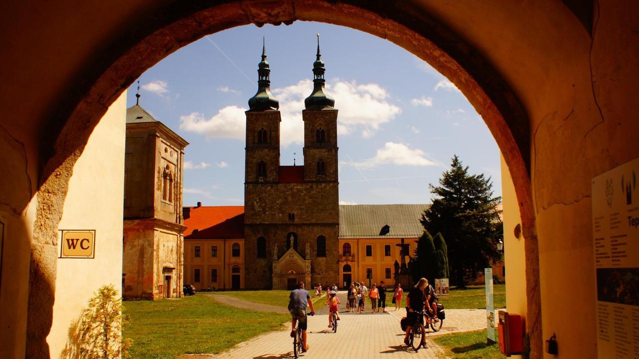 Durch ein rundes Tor fahren Radfahrer auf den Innenplatz des Klosters.
