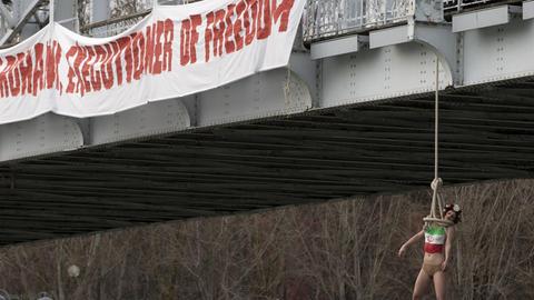 Proteste in Paris: Eine Femen-Aktivisten ließ sich in Anspielung auf die Hinrichtungen im Iran von einer Brücke über der Seine hängen. Auf einem Transparente daneben steht: "Willkommen Rohani, Henker der Freiheit."