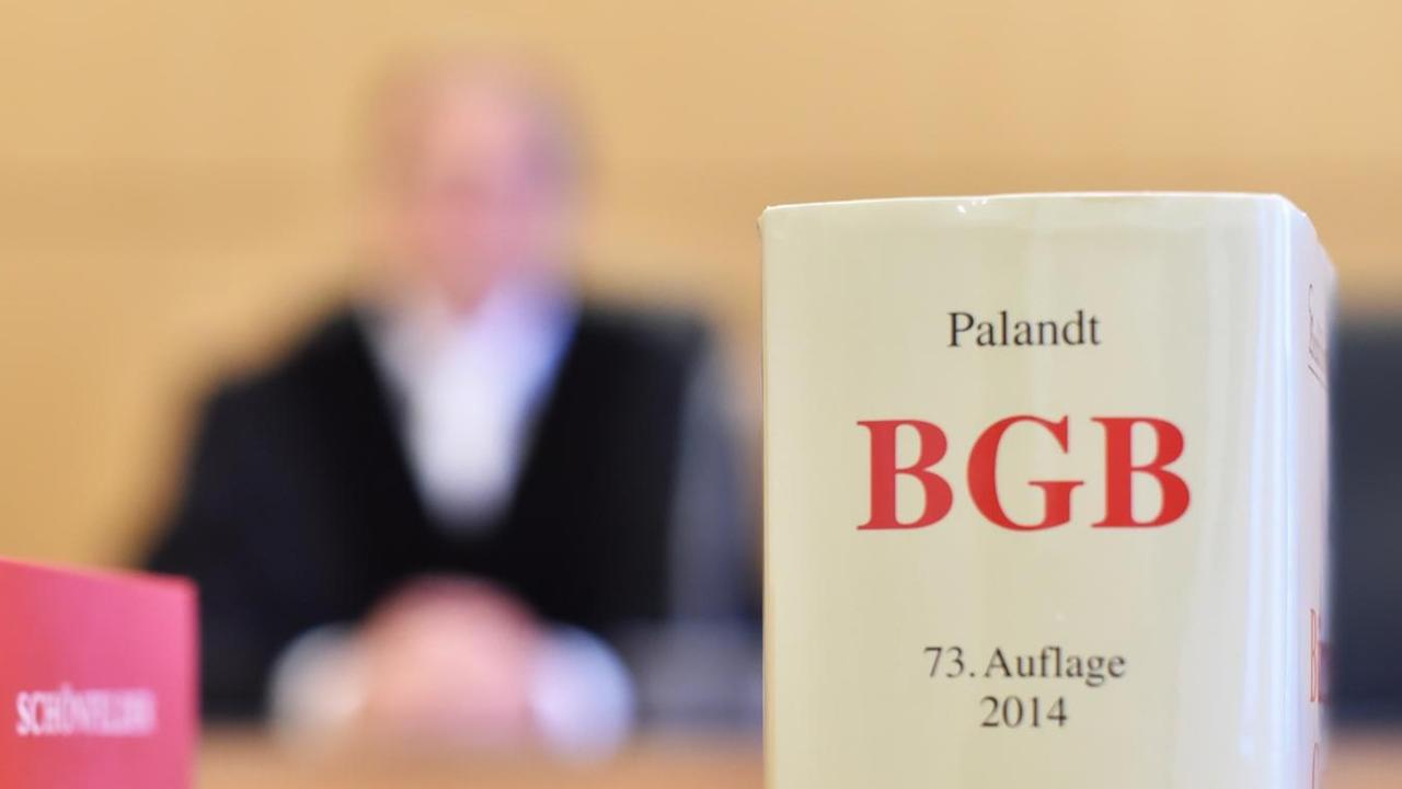 An der Richterbank eines Sitzungssaals sitzt ein Richter mit Richterrobe, davor stehen Gesetzesbücher. An der Richterbank eines Sitzungssaals sitzt ein Richter mit Richterrobe, davor stehen Gesetzesbücher.