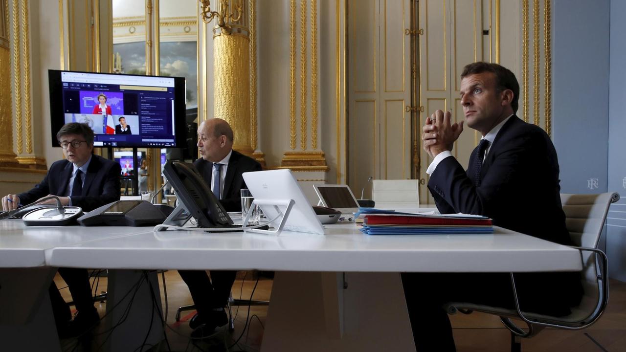 Frankreich, Paris: Emmanuel Macron (r), Präsident von Frankreich und Jean-Yves le Drian (M), Außenminister von Frankreich, nehmen im Pariser Elysee-Palast an einer internationalen Videokonferenz über Impfungen teil.