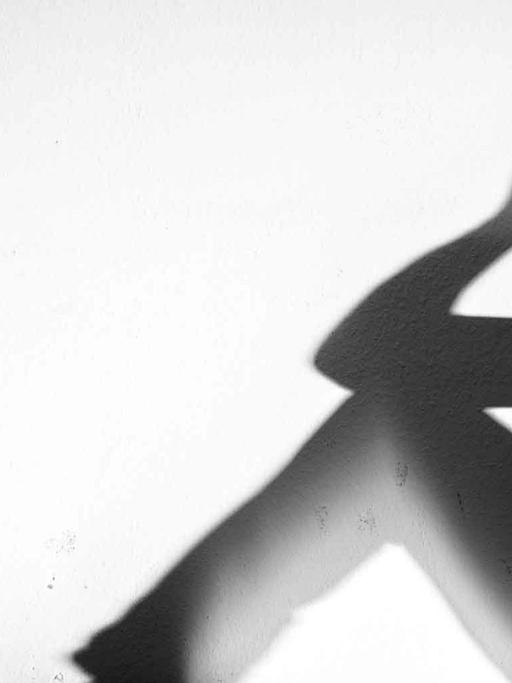 Ein Mensch sitzt auf einer Fensterbank und stützt seinen Kopf mit den Armen, im Gegenlicht sind nur seine Umrisse erkennbar.