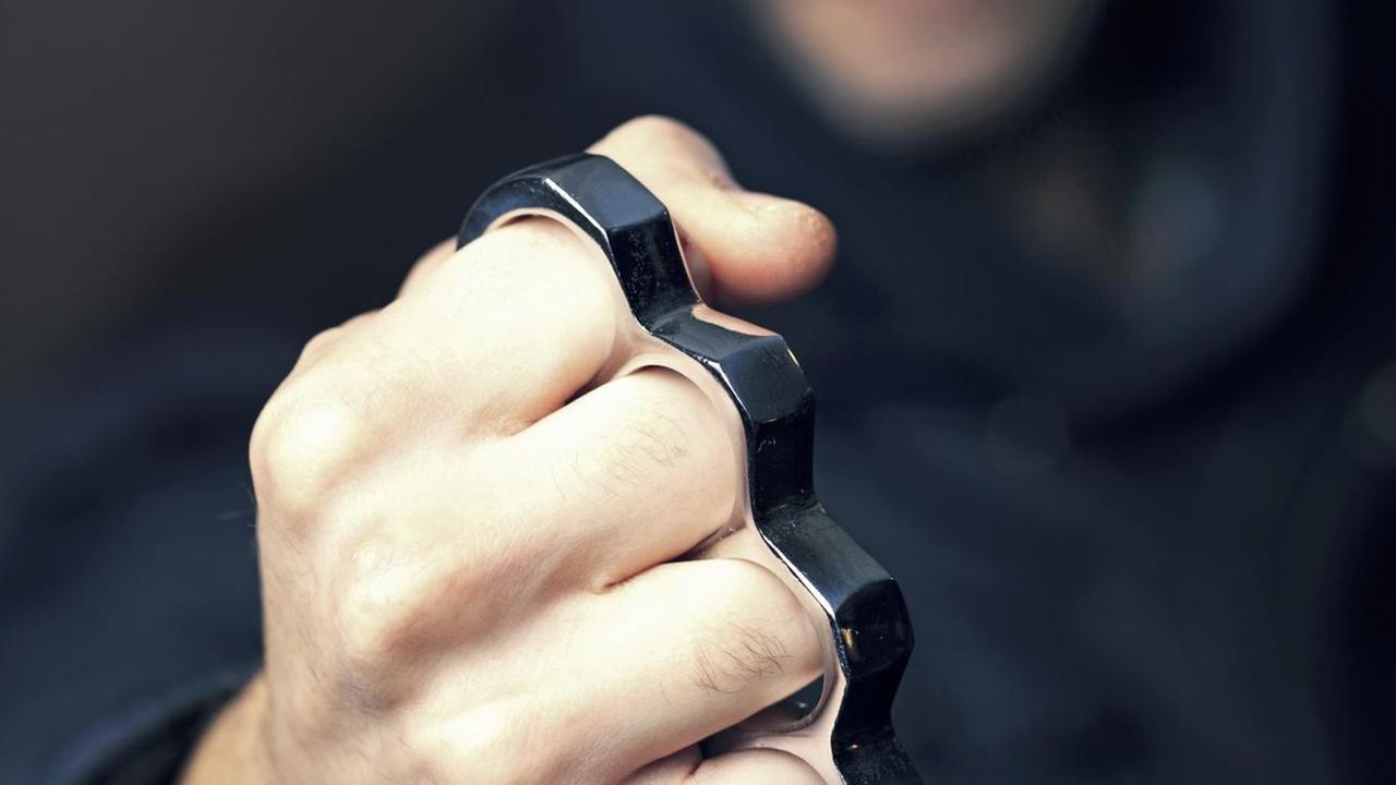 Ein Mann in einem dunklen Kapuzenpulli hält einen Schlagring in der Hand. Ein Mann in einem dunklen Kapuzenpulli hält einen Schlagring in der Hand.