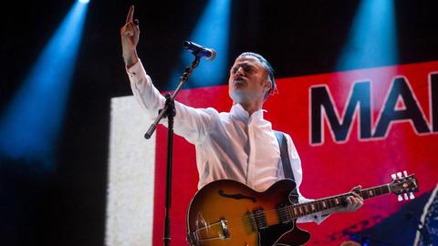 Sänger Björn Dixgård steht mit einer Jazzgitarre in weißem Hemd auf der Bühne und reckt den Arm empor.
