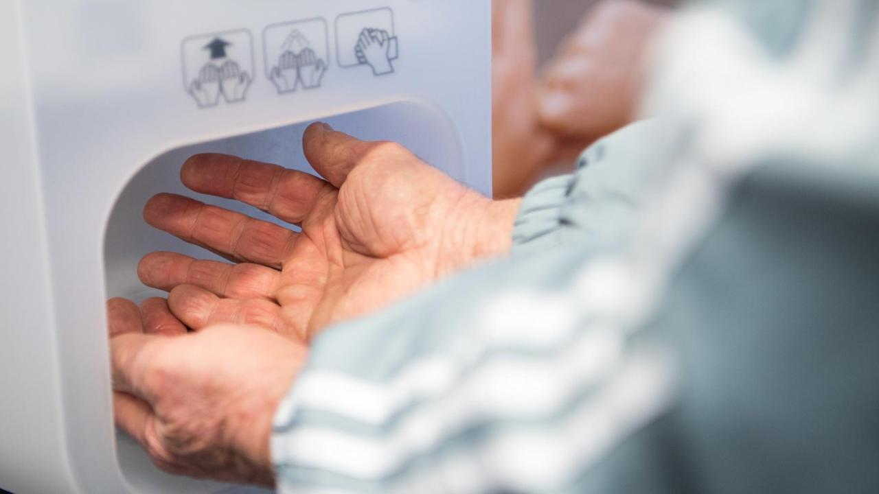 Ein Mann desinfiziert im Eingangsbereich einer Klinik seine Hände. Ein Mann desinfiziert im Eingangsbereich einer Klinik seine Hände.
