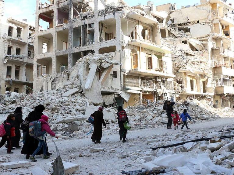 Syrische Familien auf der Flucht aus Ost-Aleppo - im Hintergrund sind zerstörte Gebäude zu sehen.