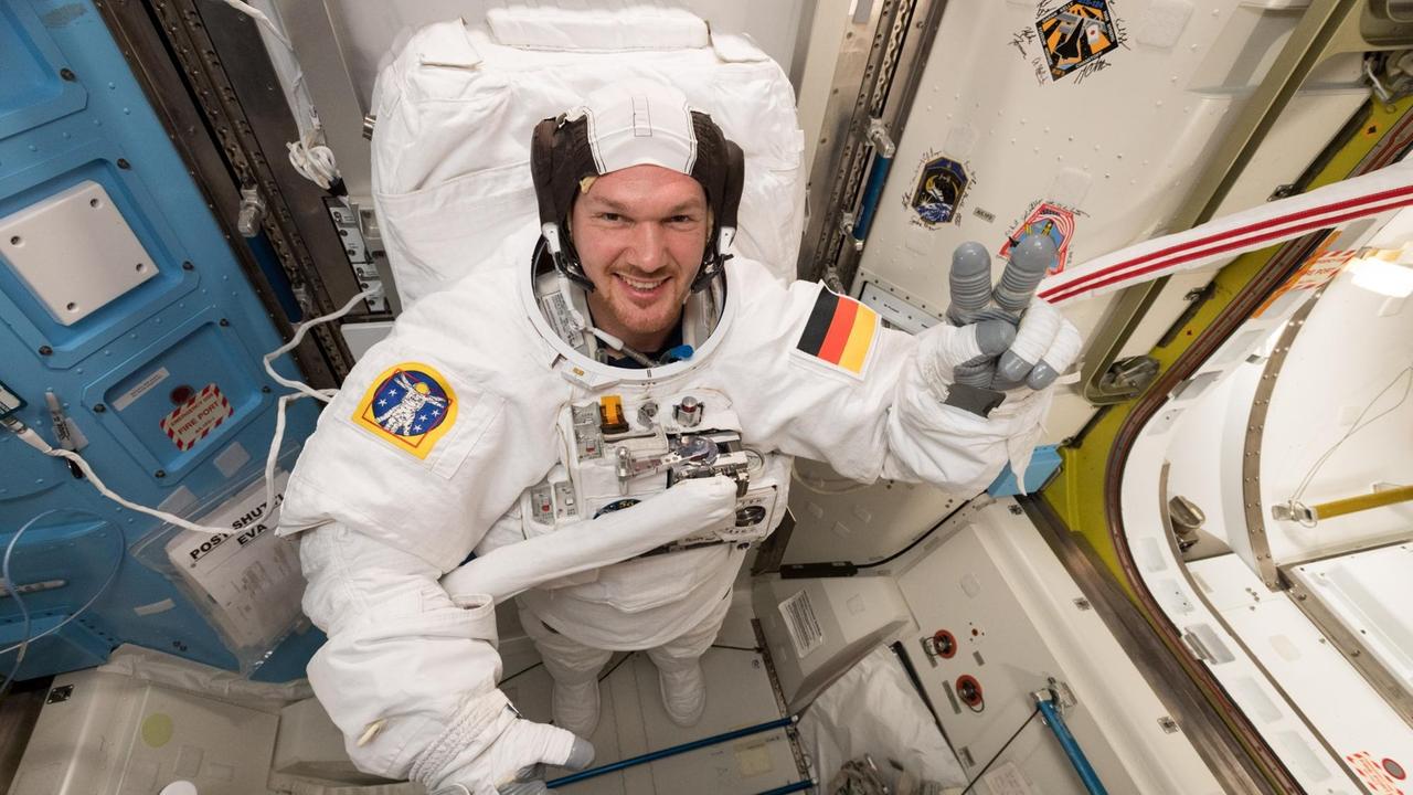 Alexander Gerst hat einen Astronautenanzug an und zeigt mit der linken Hand das "Victory"- bzw. "Peace"-Zeichen. Alexander Gerst hat einen Astronautenanzug an und zeigt mit der linken Hand das "Victory"- bzw. "Peace"-Zeichen.