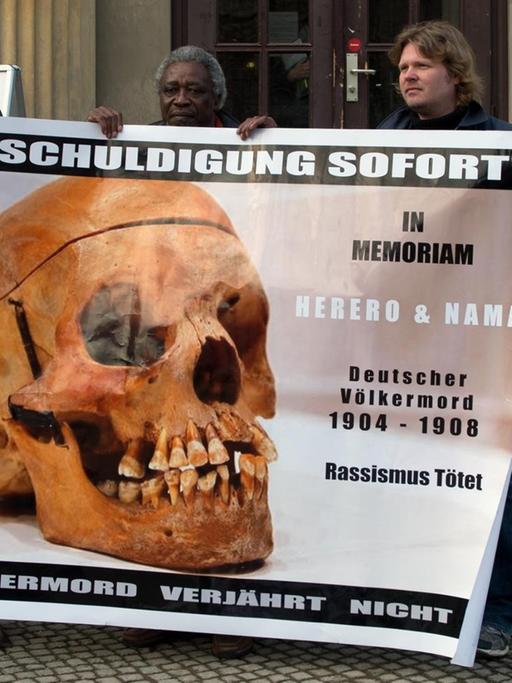 Demonstranten mit einem Transparent "Entschuldigung sofort - Völkermord verjährt nicht" vor einem Gebäude der Charite in Berlin