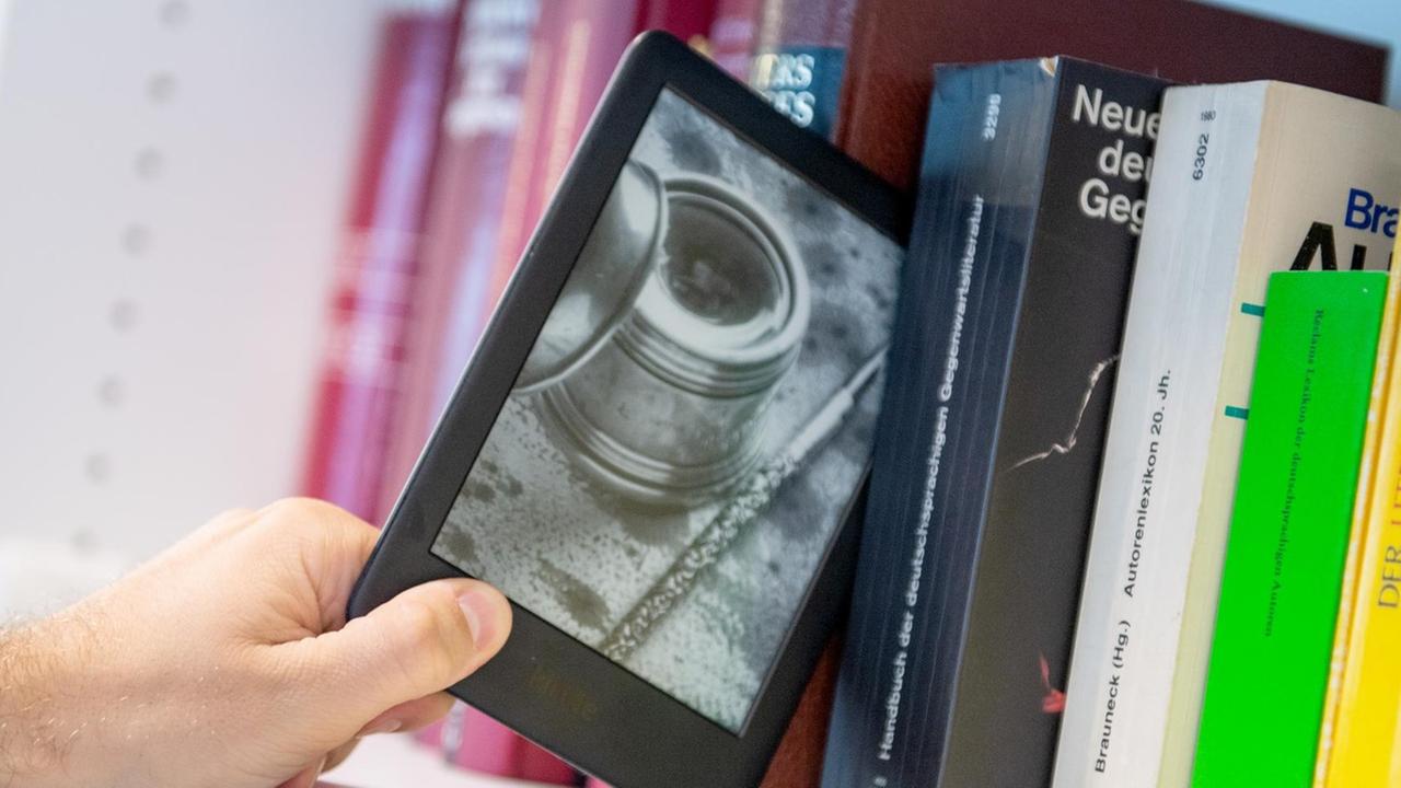 Ein Mann entnimmt ein E-Book-Reader aus einem Bücherregal Ein Mann entnimmt ein E-Book-Reader aus einem Bücherregal