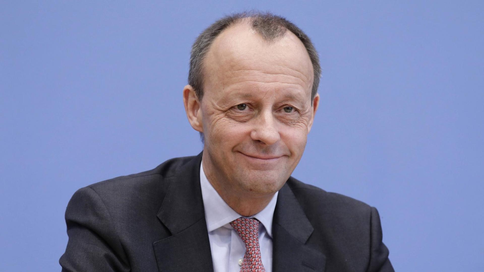 Friedrich Merz äußert sich in der Bundespressekonferenz in Berlin zu seiner Kandidatur für den CDU-Parteivorsitz. Er sitzt vor einer blauen Wand und grinst. Friedrich Merz äußert sich in der Bundespressekonferenz in Berlin zu seiner Kandidatur für den CDU-Parteivorsitz. Er sitzt vor einer blauen Wand und grinst.