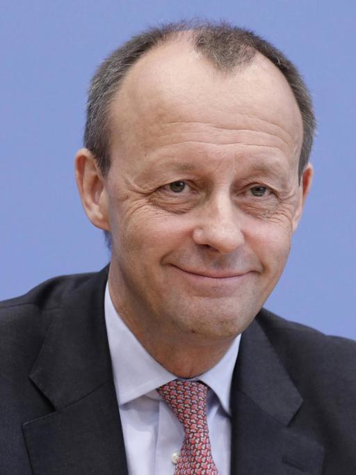 Friedrich Merz äußert sich in der Bundespressekonferenz in Berlin zu seiner Kandidatur für den CDU-Parteivorsitz. Er sitzt vor einer blauen Wand und grinst.