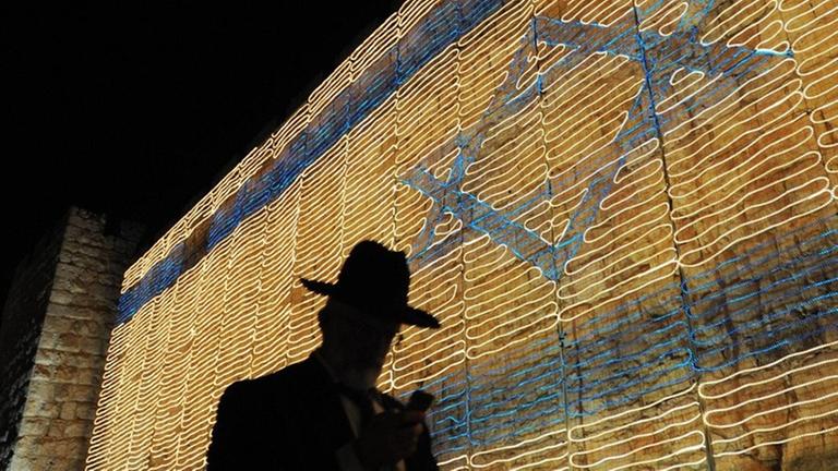 Ein Mann mit großem Hut steht vor einer israelischen Flagge