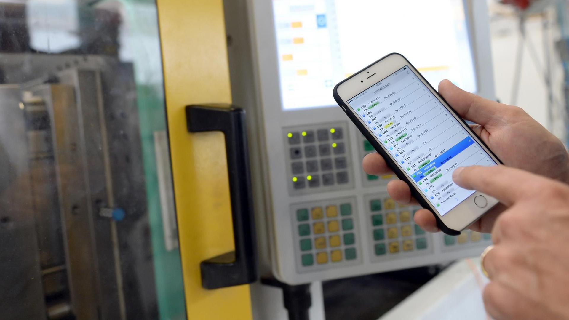 Geschäftsführer Thomas Dreusicke des Kunststoffverarbeiters India Dreusicke zeigt am 08.10.2015 in Berlin in der Fertigungshalle auf einem Smartphone die Überwachung der Maschinen.