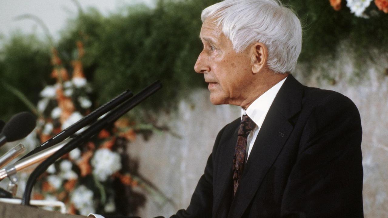 Ernst Jünger steht seitlich zur Kamera und spricht in ein Mikrofon. Ernst Jünger steht seitlich zur Kamera und spricht in ein Mikrofon.