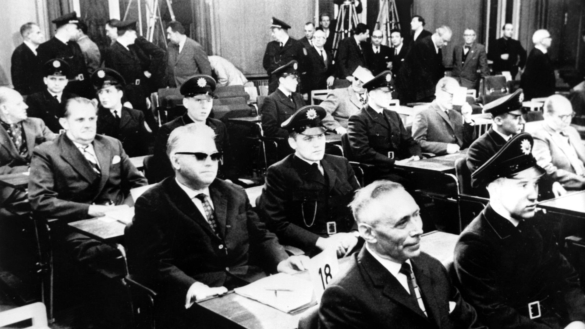 22 ehemalige Wachen und Beamte des Konzentrationslager Ausschwitz stehen im Dezember 1963 in Frankfurt vor Gericht.