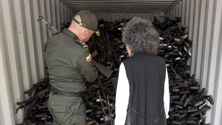Die kolumbianische Künstlerin Doris Salcedo steht zusammen mit einem Mann in Uniform vor einem geöffneten Lieferwagen voller Maschinengewehre, die die FARC im Rahmen des Entwaffnungsprozesses abgegeben hat. Die kolumbianische Künstlerin Doris Salcedo steht zusammen mit einem Mann in Uniform vor einem geöffneten Lieferwagen voller Maschinengewehre, die die FARC im Rahmen des Entwaffnungsprozesses abgegeben hat.