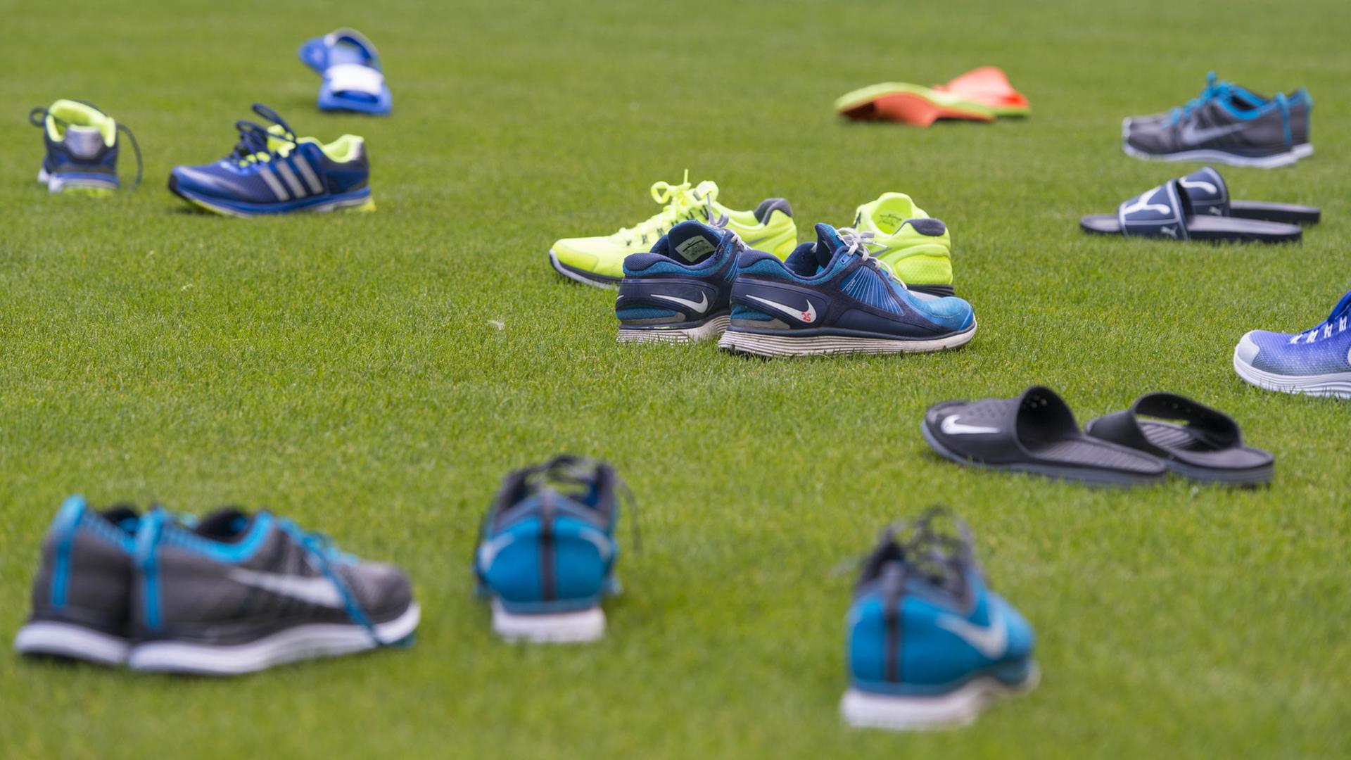 Auf einem Fußballfeld liegen mehrere Paar Sportschuhe und Badesandalen aus Plastik. Auf einem Fußballfeld liegen mehrere Paar Sportschuhe und Badesandalen aus Plastik.