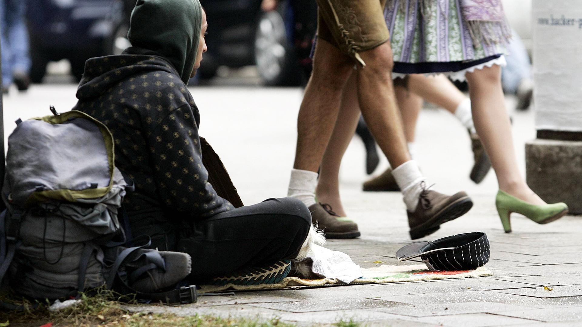 Bettelnder Obdachloser sitzt auf einem Bürgersteig, während Wiesnbesucher in Tracht achtlos an ihm vorbeigehen. Bettelnder Obdachloser sitzt auf einem Bürgersteig, während Wiesnbesucher in Tracht achtlos an ihm vorbeigehen.