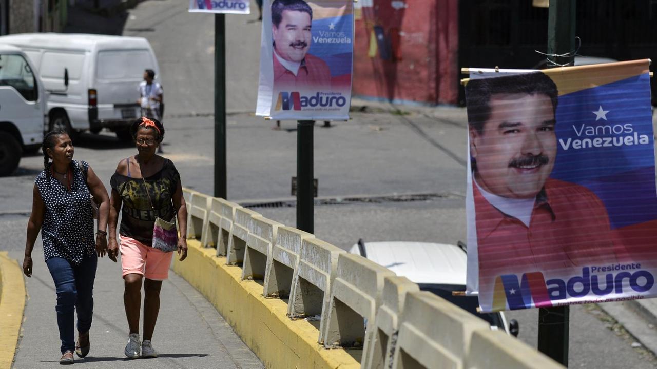 Frauen laufen eine Straße in Caracas entlang, die von Wahlplakaten des Präsidenten Nicolas Maduro gesäumt ist