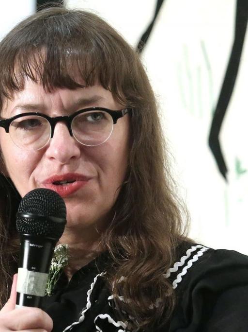 Comiczeichnerin Ulli Lust sitzt auf eine Podium. Eine Frau mit langen dunklen Haaren und einer Brille.