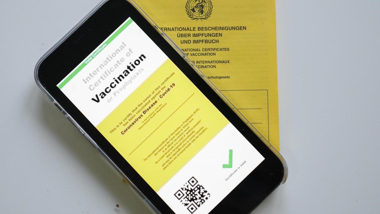Symbolbild eines möglichen digitalen Impfpasses mit einem analogen gelben Impfpass Symbolbild eines möglichen digitalen Impfpasses mit einem analogen gelben Impfpass